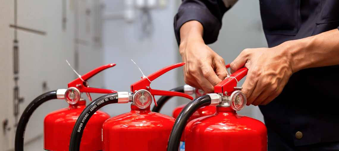 Hände bei der Kontrolle und Sicherung mehrerer roter Feuerlöscher in einem technischen Arbeitsumfeld.