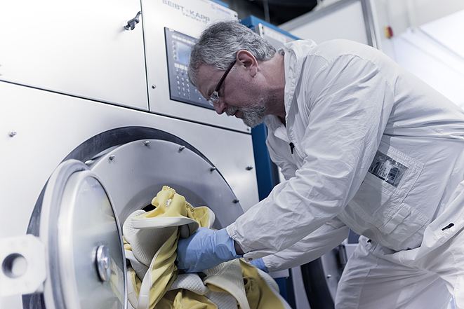 Ein Mitarbeiter der Firma BTI in Schutzkleidung und mit Schutzhandschuhen befüllt eine Industriewaschmaschine mit vorgereinigten Materialien.